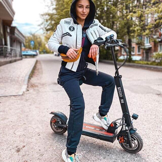 Una joven posa con su Kugoo en una avenida. Los patinetes Kugoo son la mezcla perfecta entre elegancia, transporte y aventura